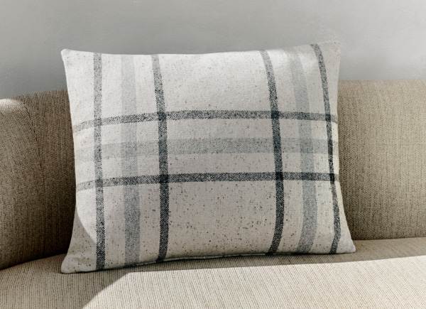 A singular rectangular pillow with knife edge seam placed on a neutral couch against a white wall 