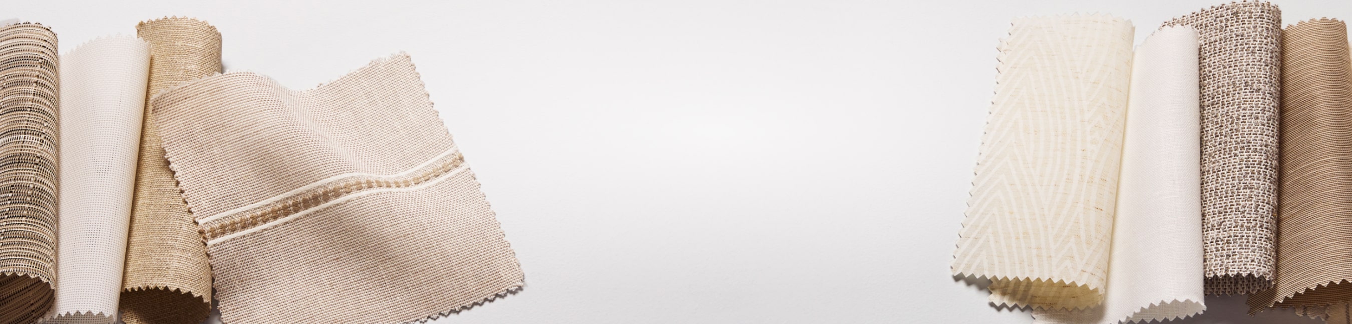 An assortment of fabric swatches for window treatments in a range of neutral hues displayed on a table.