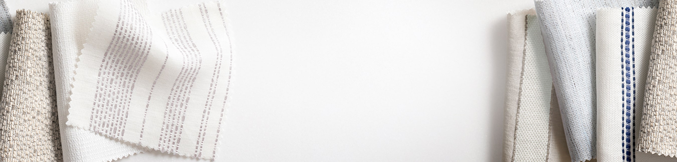 An assortment of fabric swatches for window treatments from the Victoria Hagan collection displayed on a table.