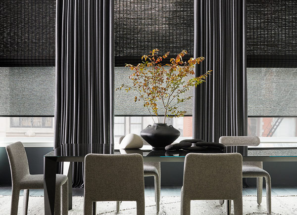 Large windows featuring solar shades layered under roman shades and drapery in a Dining Room with a table and plush chairs