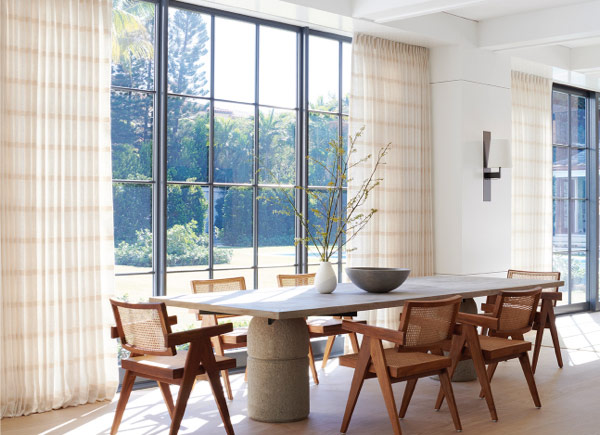 Floor to ceiling windows featuring Tailored Pleat Drapery in Lily Buff in a dining room with a stone table and wood chairs