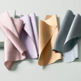 Various swatches from The Shade Store in materials Silk Dupioni, Techno and Raw Silk on a light green table with a block