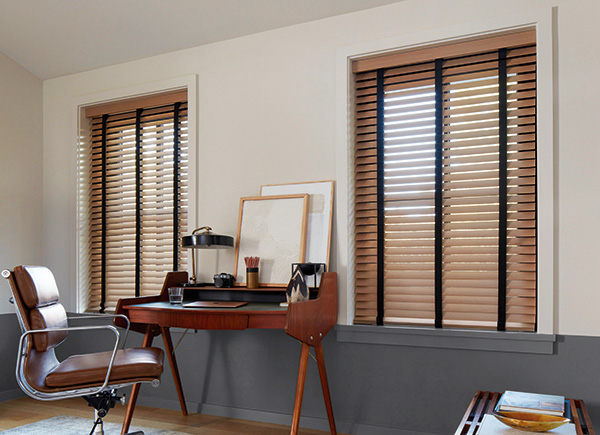 Two windows featuring wood blinds in and office with a brown chair and centered wood desk against grey and white walls