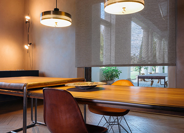 A large window featuring woven wood shades in grassweave toast in a kitchen with a large wood table and brown chairs