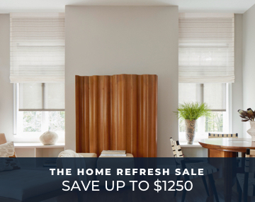 Two tall windows featuring motorized roller shades in a dining room with seating & large centered brown art with promo text