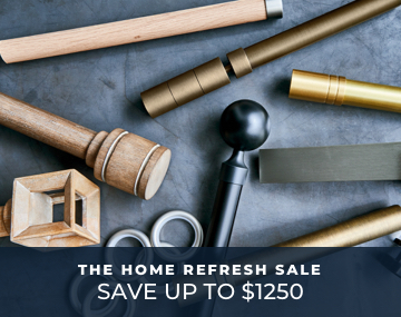 Various pieces of drapery hardware in multiple metal and wood finishes laid on a cement table with Home Refresh Sale text