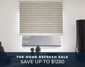 Pleated Roman Shade hung over a Roller Shade on large window with a large white table and large black vase with promo text