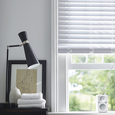 A window featuring a Faux Wood Blind in 2 inch Faux Blanc in a bathroom with white walls and a black table with a table